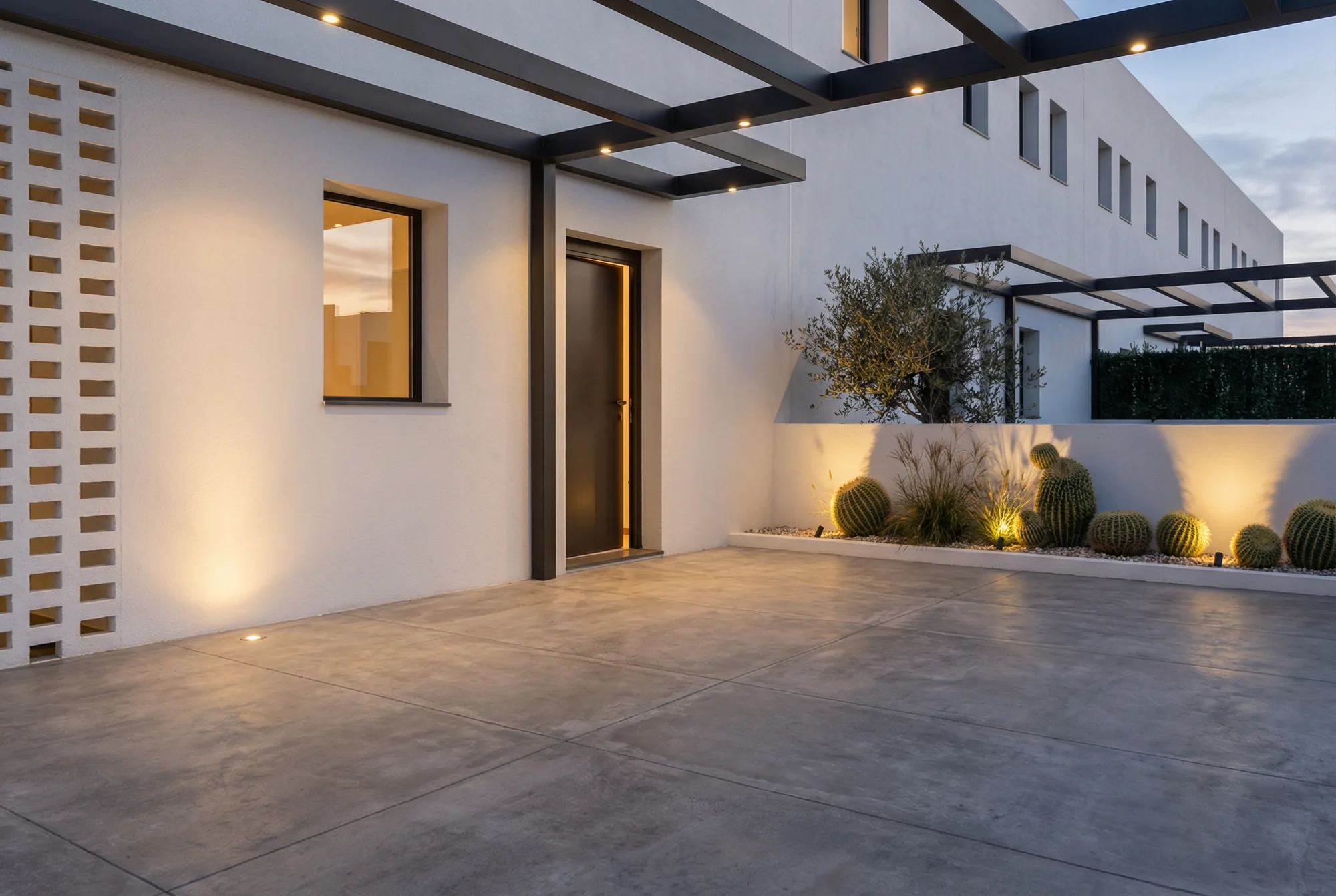 Acceso exterior de una vivienda bajo una pérgola con iluminación integrada